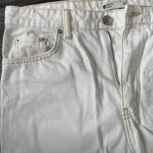 Vita jeans med bruna sömmar, i modellen ”momjeans”. Två fickor framtill samt två fickor baktill.