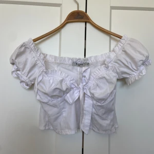 Vit topp - Vit super gullig topp från NA-KD, croppad i modellen med puffärmar som går lika bra att bära offshoulder. Band som knytes mellan brösten och en osynlig dragkedja från vänster armhåla och hela vägen ned. Nästan aldrig använd, perfekt inför sommaren 🌼