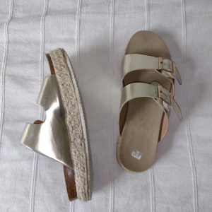 Sandaler - slip ins - guldfärgade -38/39 - Guldfärgade sandaler med snygga sulor. Har inte använts mycket, men remmarna och sulorna är lite skavda och slitna i kanterna. Storlek 39 men jag skulle säga att de är mer som 38. 