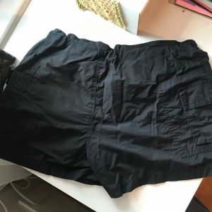 Black cargoshorts - Svarta shorts i cargo-stil. Fint skick utan defekter. Strl 38 men justerbara i midjan så passar mindre också. Sitter bra på mig som har strl S i byxor.