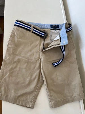 Polo Ralph lauren shorts beige  - Beige Ralph lauren shorts med blått skärp. Nypris 849kr köpt på kidsbrandstore