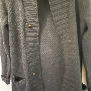 Svart kofta stickad  - En svart lång stickad kofta, storlek xs, använd en gång, den är mysig och har knappar och två fickor. Kan skickas med frakt, Swish betalning. 