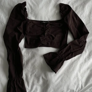 Brun croptop med volangdetaljer - Långärmad croptop med volanger. Sitter tight. Del av ett sett.