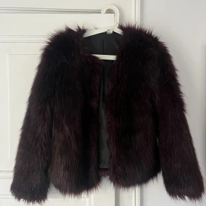 Pälsig jacka - Lila/röd/brun pälsig jacka (inte riktig päls). Kul för utekvällar!! Storlek 38 men kanske mer åt 36-hållet