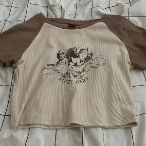 En beige crop topp med änglar på som det står ”angel baby” som är ifrån shein då den inte kommer till användning längre 