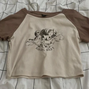 Beige crop topp - En beige crop topp med änglar på som det står ”angel baby” som är ifrån shein då den inte kommer till användning längre 