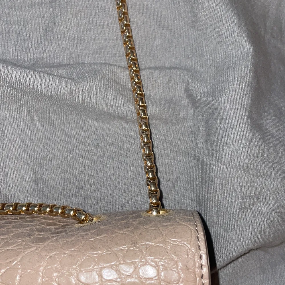 En beige/brun handväska med guld detaljer inte till användning, super fin att ha till klänning . Väskor.