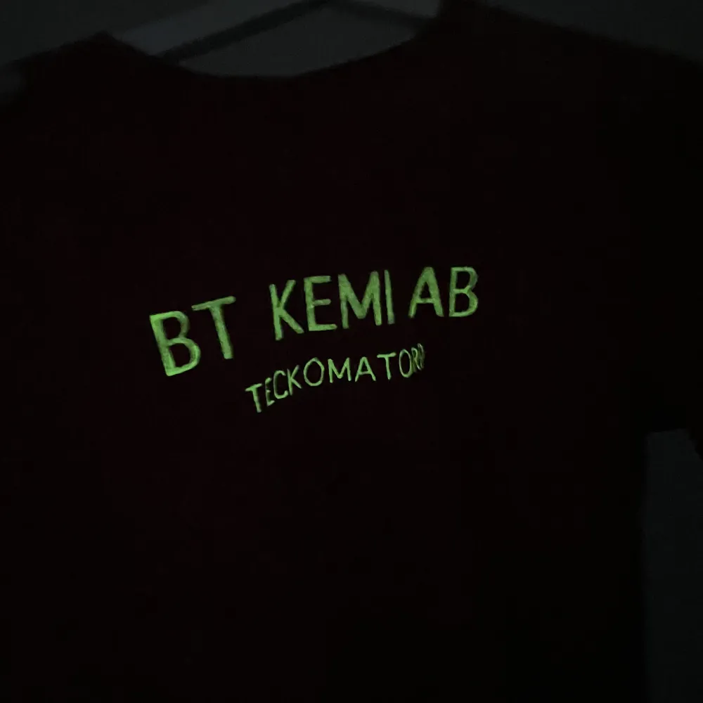 En styck tshirt med självlysande BT-Kemi AB-tryck på bröstet.  Med en design som ser ut att vara tämligen nedstänkt av Dinoseb eller något annat livsfarligt.. T-shirts.