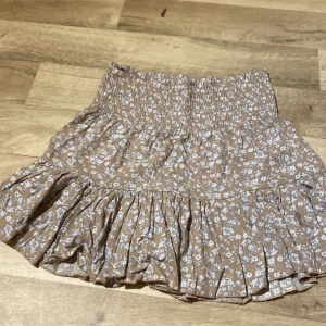 Blommig kjol, lager 157 - En fin blommig kjol från lager 157 i storlek S, ny så bara använd cirka 3-5 gånger. Säljer pga att den e för stor. Beige med blå vita blommor.
