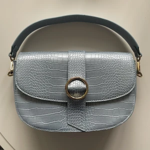 Unik ljusblå NA-KD väska - Väldigt fin ljusblå väska av märket NA-KD som tyvärr aldrig kommit till använding. Helt ny, oanvänt. Har en extra längre väska "strap", kan användas både som cross-bag och handbag. Rymmer mycket. Har en original dust bag/dammpåse.  (Blåare i verkligheten)