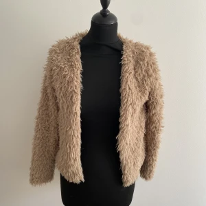 Fluffig kofta beigebrun  - Fluffig beigebrun kofta från Gina tricot i Strl XS. Storleksklass saknas och är i använt men gott skick. Viss tvättpulvernas kan synas på ’fluffet’ i förhållandentill den andra annonsen med samma kofta i vit. 