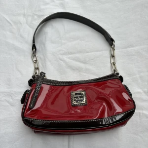 Väska  - Cool liten röd väska från det exklusiva märket dooney & bourke, har tuschmarkeringar på vissa ställen 
