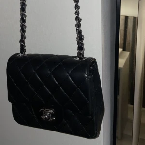 Liten svart väska  - Liten svart väska. Med silver detaljer och lång axelremskedja. Aldrig använd.