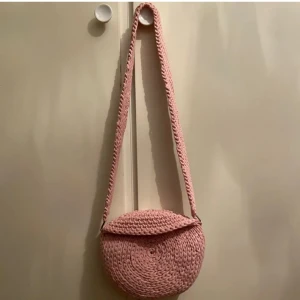 Väska - Rosa virkad väska. Överlappningarna kan väcklas upp men blir då inte lika rund som jag hade önskat därav nerväcklingen, vilket funkar lite som en stängning till väskan. längd: 21cm höjd: 18cm bredd: 9.5cm 