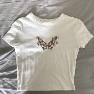 En jättefin vit croppad t-shirt med ett brunt fjärils tryck på. Säljer denna då den inte är min stil längre. Jättefint skick och har inte används många gånger.