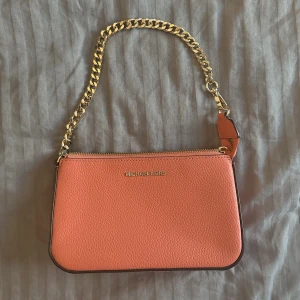 Michael Kors väska - En liten och supersöt Michael Kors väska som aldrig kommit till användning. Bilderna ger inte en rättvis bild av färgen, men verkligen så fin korallfärg. Äkta självklart. Köpt för runt 1000kr säljer för 700kr! 💓