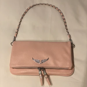 Zadig & Voltaire väska rosa - Ljusrosa Zadigväska som är helt nyköpt och oanvänd. Köpte den utomlands till ett hyfsat lågt pris jämfört med originalet, så den är förmodligen fake. Däremot känns materialet och kvaliten väldigt bra. Extra längre axelband tillkommer. Svar på frågor i DM.