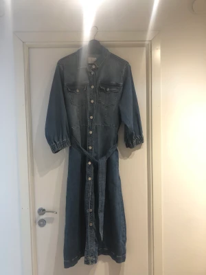 Jeansklänning - Fin jeansklänning med bälte i storlek L från Love & Divine. Köpt på Magasin i Köpenhamn och endast använd ett fåtal gånger. Läng 126 cm  