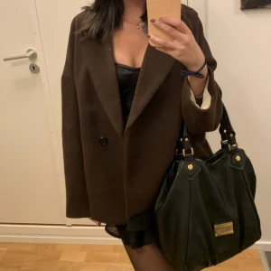 Kort kappa - Säljer denna fina bruna korta kappa! Den är i fint skick men finns tecken på användning då den använts en del, finns en defekt på ärmen på insidan och i vänster ficka, ett litet hål på innertyget men det är inget som syns. Frakt ingår i priset ❤️