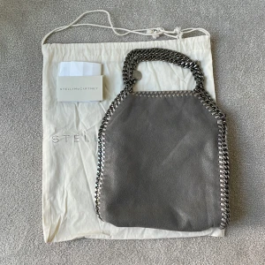 Stella McCartney väska - Jättefin ”Falabella Mini Tote Bag” köpt på Vestiaire Collective med tote bag och kvitto. Väskan har tecken på användning som ni kan se på bilderna. Idag kostar en ny 10,180kr och jag säljer för 4000kr🩵