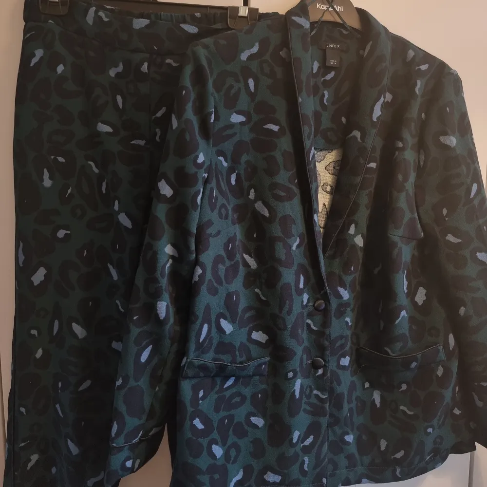 Mörkgrönt leopardmönstrat kostymset från Lindex. Cigarettbyxor med revär och fickor fram och bak. Kavaj med knappar och sydda fickor. Storlek M i kavaj och byxor i storlek S.. Kostymer.