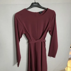 Vinröd/lila klänning från bubbleroom storlek 36 - Lila/röd klänning med knytbar detalj som är jättefin att knyta i ryggen. Dragkedja i ryggen. Gjord av 100% polyester. Säljs då den inte passar längre. Använd ett fåtal gånger. Kommer från ett rökfritt hem. 
