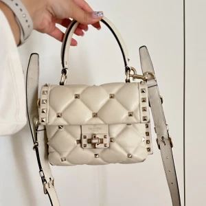 Valentino Garavani  -   Så snygg Valentino väska i modellen candystud i en off-white färg som inte längre säljs. I den mindre storleken. Kommer med axelband och är i bra skick men lite slitningar på kanterna. Kommer med dustbag, kvitto och intyg. 