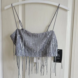 Glittrig topp - Supersnygg glittrig topp från NAKD. Den är helt ny, endast provad en gång! Lappar sitter kvar. Jag säljer även den matchande kjolen till. Du får hela settet för 300 kr (Nypris: 229kr + 549kr) Storlek M