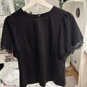 Svart topp med spets - Svart kortärmad topp med spets på ärmarna. Storlek S, men passar också M. Aldrig använd!