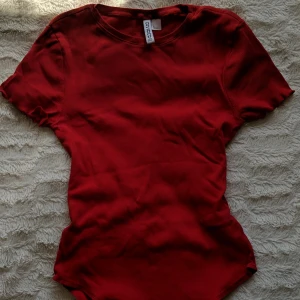Röd tshirt body  - En ribbad body, klarröd färg. Nästintill oanvänd 