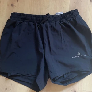 Träningsshorts - Shorts från Ronhill i storlek XS, aldrig använda då dom var lite tajt på mig. Tajtare short under och lite pösigare yttre (2 lager) 