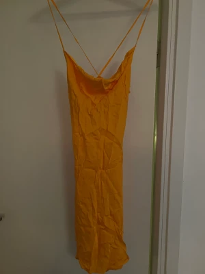 Satinklänning - Den är aldrig använd då den är lite för kort för mig. Annars är den otroligt fin och passar väldigt fint till fest och till sommaren. Den har öppen rygg med kryss med banden.  Den är skrynklig men jag stryker den självklart innan jag skickar den.