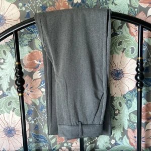 Gråa Ellos Kostymbyxor - Fina byxor i tjockt tyg och ordentliga sömmar. Oanvända, endast tvättade. Hög midja som ska sitta åt runt höften och har vida långa ben. Färgen är som första bilden. Innerbenslängd 77cm, midja 70cm. Tvätt 40° får ej torktumlas. 