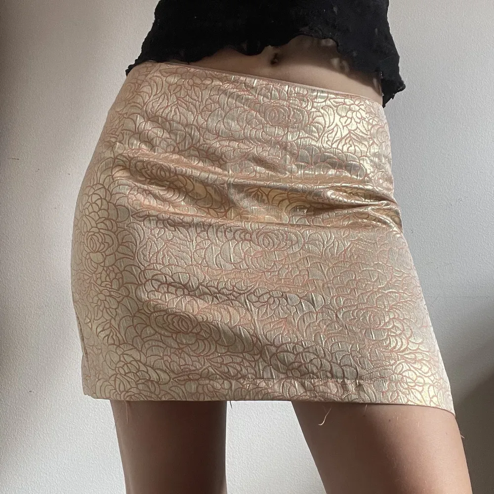 Kort kjol i guld med rosa/beige blommigt mönster. Den är uppsydd lite av mig. Jag är 165 cm och brukar ha storlek s-m. Kan mötas nära Mariatorget. . Kjolar.