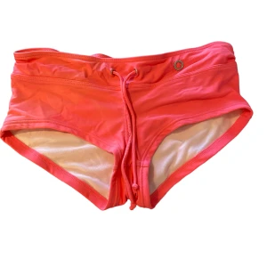 Rosa badtrosa/shorts RÖHNISCH - Köptes för ca 6 år sedan och användes bara 2 gånger då den inte föll i min smak. På vänster sida finns lite missfärgningar och på etiketten. På baksidan finns det små svarta prickar som märks knappt men på det hela i bra skick!  (82% Polyamid, 8% Elastan)
