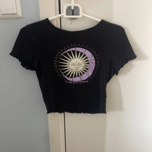 Croppad topp med tryck  -  Croppad topp svart med ett tryck månen och solen.Använt ett få tal gånger, säljer då den inte har kommit till användning på senaste tiden, från hm