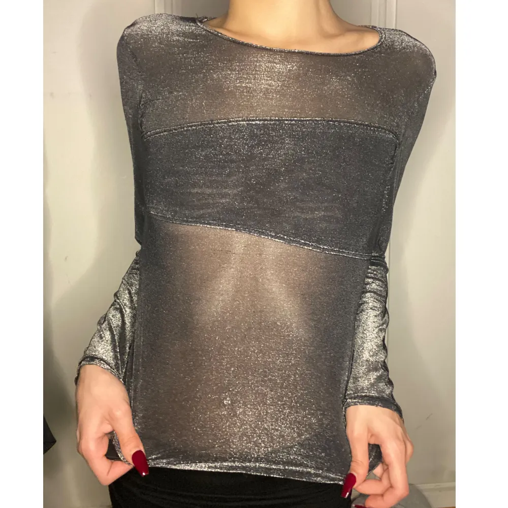 Glittrig tröja i mesh, genomskinlig rygg samt framme på magen och ärmarna. Tjockare mesh som inte är helt genomskinligt över bröstet . Toppar.