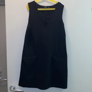 Klänning  - En svart, stilren klänning med fickor  och en snygg V-ring. Använd flitigt men är i gott skick.