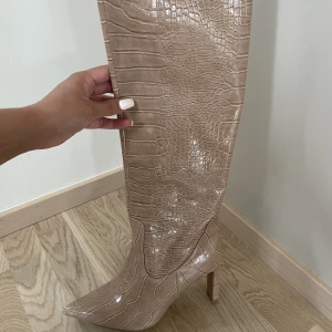 Höga boots NA-KD med klack  - Höga boots med brett skaft som går under knät med klack i beige  ”ormskinn”. Klackhöjd 8.5cm. Använda vid 2 tillfällen ute. 