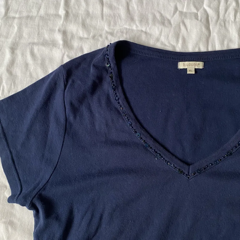 Mörkblå T-shirt med snygg pärldetalj, köpt secondhand och har en liten fläck strax under nyckelbenet men inget som stör!! Annars i bra skick🌷. T-shirts.