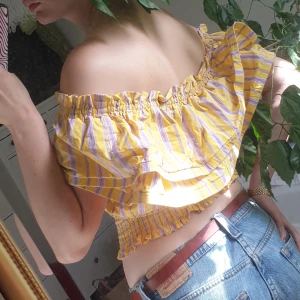 Finaste Statement Toppen - Hur ska jag ens beskriva denna pärla? Gul/lila- randig volangtopp som kramar midjan lätt. Volangen har extra volym på ena sidan vilket ger den en elegant look, går att bära den delen över axeln. Toppen är superbekväm och mjuk, går verkligen att styla!