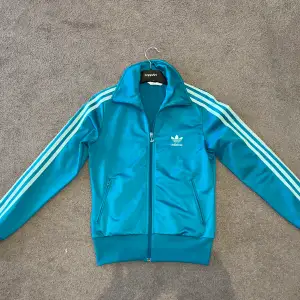 En superfin turkos adidas zip tröja i storlek xs för dam men själva modellen passar lika bra för killar men den är bara lite liten om man jämför med herr storleken xs. Bra skick 9/10. Tveka inte på att ställa frågor