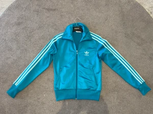 Turkos Adidas Zip Tröja - En superfin turkos adidas zip tröja i storlek xs för dam men själva modellen passar lika bra för killar men den är bara lite liten om man jämför med herr storleken xs. Bra skick 9/10. Tveka inte på att ställa frågor