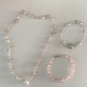 Rosa smyckes-set av ett halsband och två armband. Gjorda av glas, plast, rosenkvarts, vit Sten och elastisk tråd. Armband 5-6cm i diameter  Halsband 24-16cm i diameter. Handgjort. Köpare står för frakt.