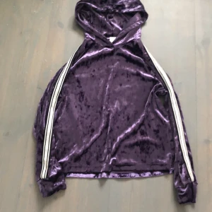 Lila sammets hoodie  - Jag säljer en lila sammets tröja men silver ränder på armarna. Tyget är ganska tunt. Tröjan är i bra skick. Skriv till mig för fler bilder eller frågor😊
