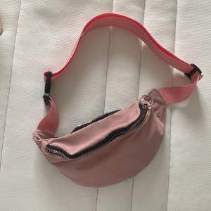 En rosa väska med tjocka band som funkar som både mag- och axelväska. Aldrig använd! (Axelbandet är justerbart)  Finns även en gömd inneficka🩷