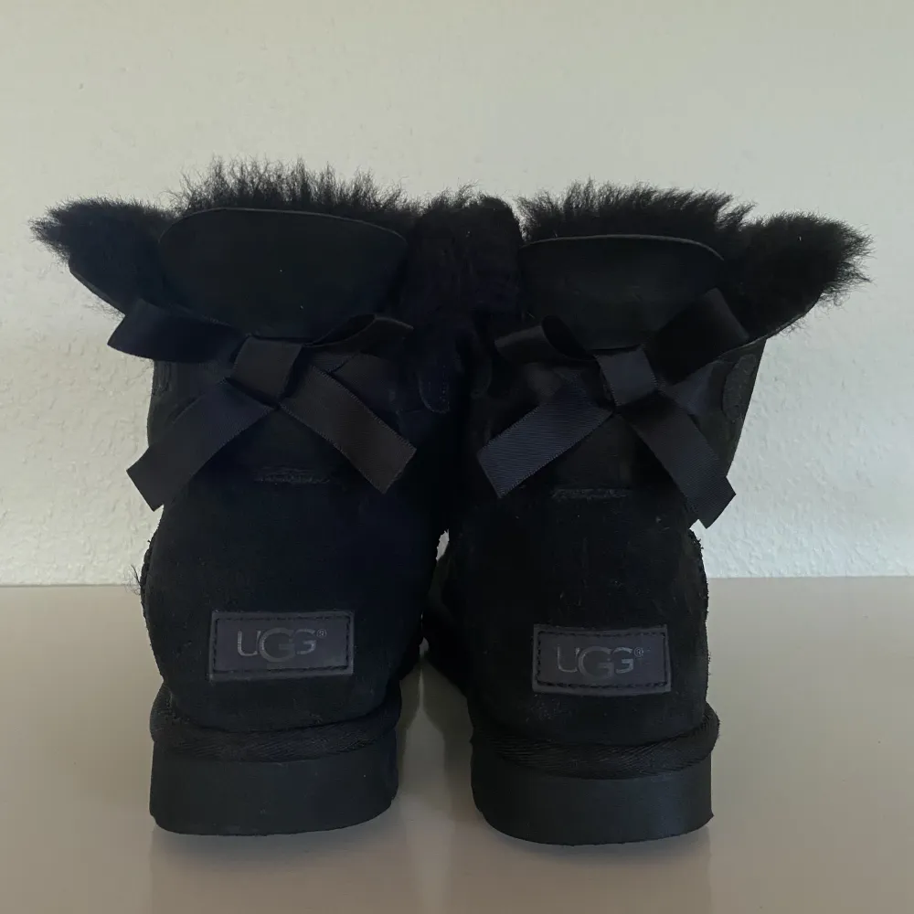 Ett par svarta ”mini bailey bow” från märket UGG i storlek 39. Köpta i en UGG-butik i USA för några år sedan. Skorna har vissa tecken på användning men i övrigt i bra skick! Skriv gärna för fler bilder, så kan jag visa ”defekterna” <3. Skor.