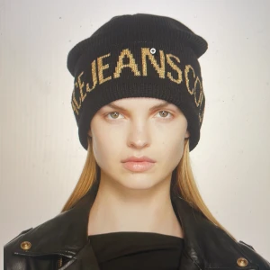 Jätte snygg och varm mössa - Denna elegant utformade mössa från Versace Jeans Couture är speciellt designad för kvinnor och är en perfekt kombination av stil och värme. Tillverkad med omsorg i högkvalitativt ulltyg (50%), är denna mössa inte bara ett modeuttryck utan också en funktio