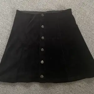 Svart kjol i manchenster med knappar som är snygga detaljer. 