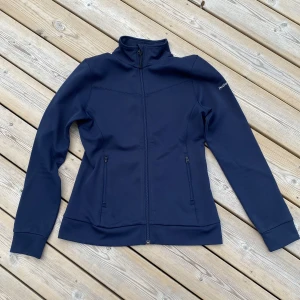 Peak Perfomance, midlayer jacket - Perfekta mellanlagerjackan för golfaren eller skidåkaren från Peak Performance, strl S. Snygg i marinblått, med vit logga på vänster ärm. Dragkedja, samt fickor fram och figursydd passform. 100% återvunnen polyester. Nyskick! 